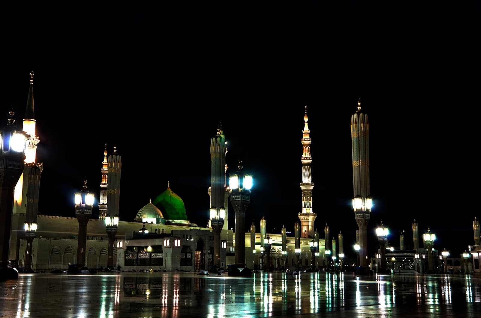 Al-Masjid an-Nabawi at night, its green dome and minarets glowing.